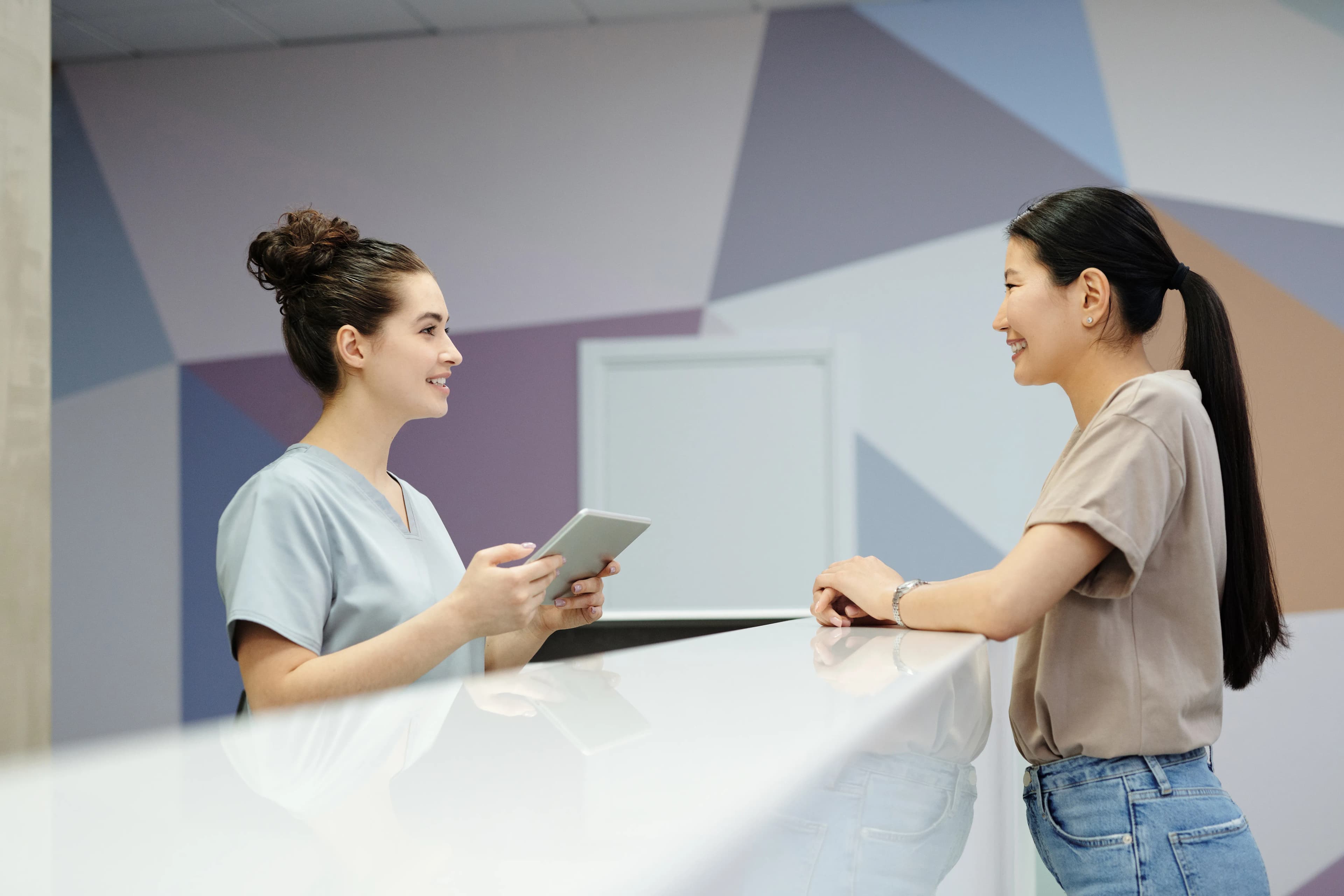 Na recepção da clínica, a recepcionista conversa sorrindo com uma paciente no balcão.